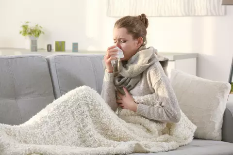 Frau niest auf dem Sofa