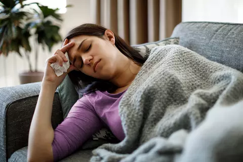 Junge Frau liegt krank auf dem Sofa – typisches Bild für Erkältung und Erschöpfung